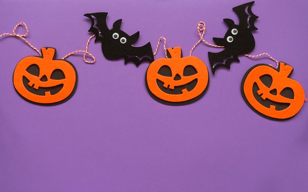 Guirnalda de calabaza y murciélago de Halloween sobre fondo púrpura