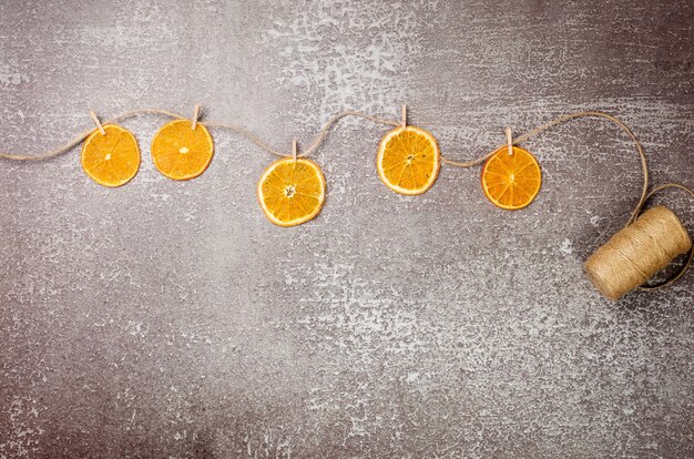 Guirnalda creativa hecha de rodajas de naranjas secas caseras con pinzas para la ropa en una cuerda de cáñamo. Navidad y año nuevo, composición de invierno. Vista superior, endecha plana, espacio de copia