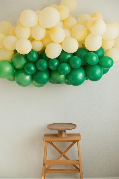 Una guirnalda de globos cuelga en la pared de una escalera de tijera y un puesto de pasteles de madera vacío