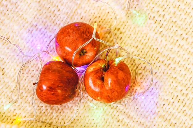 Foto guirnalda de luces de navidad y frutas frescas de manzana roja madura sobre fondo de tejido de punto.