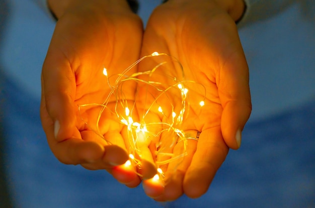Foto guirnalda que brilla en las manos de las mujeres luces navideñas en las palmas comodidad