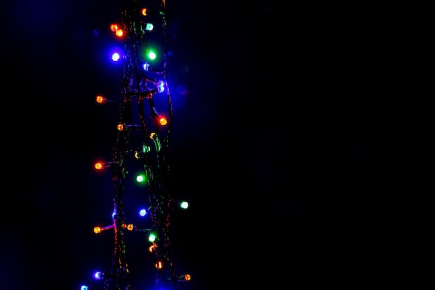 Guirnaldas de luces multicolores de Navidad y Año Nuevo en un espacio de copia vertical de fondo negro