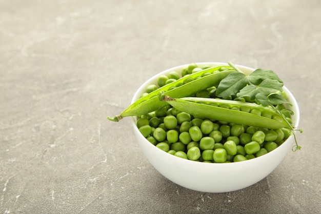 Guisante verde en un tazón sobre fondo gris. Verduras frescas orgánicas. Alimentación saludable.