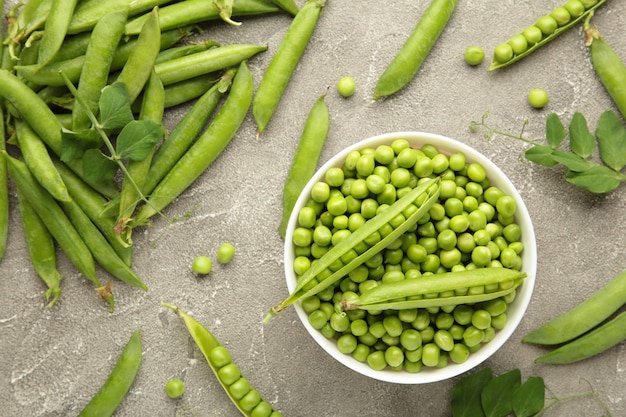 Guisante verde en un tazón sobre fondo gris. Verduras frescas orgánicas. Alimentación saludable.