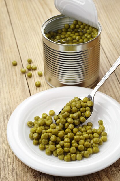 Guisantes enlatados en cuchara y plato sobre mesa de madera