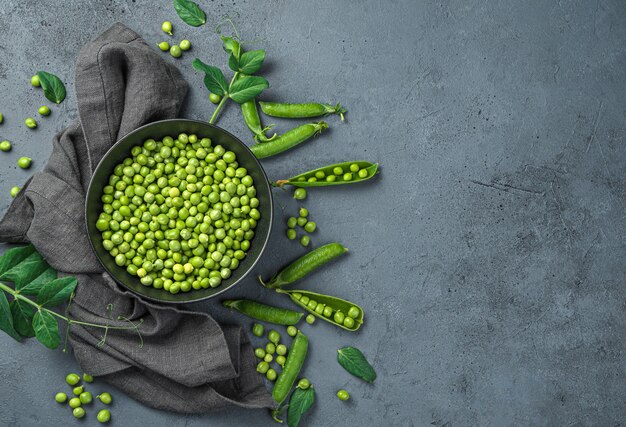 Guisantes pelados en un cuenco y vainas sobre un fondo gris. Vista superior, espacio de copia.