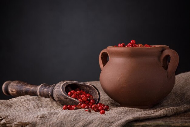 Guisantes de pimiento rojo en una cuchara de madera y olla de cerámica sobre la mesa. Fondo oscuro.