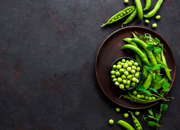 Guisantes en un tazón con vainas frescas sobre la superficie de hormigón negro