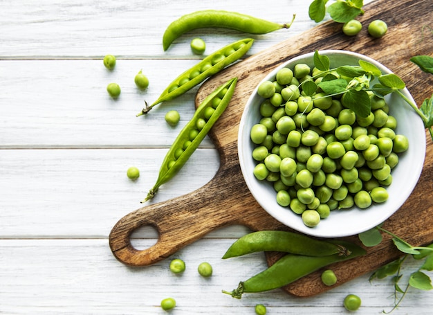 Guisantes en tazones blancos con vainas frescas sobre la mesa, vista superior o endecha plana