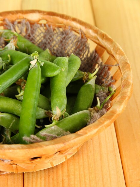 Guisantes verdes en cesta sobre mesa de madera