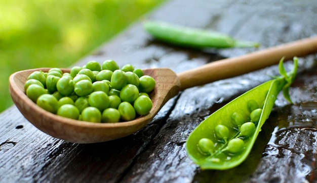 Guisantes verdes en una cuchara de madera y al lado de una puntada abierta