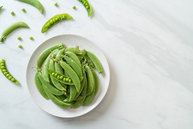 Guisantes verdes dulces frescos en la placa blanca.