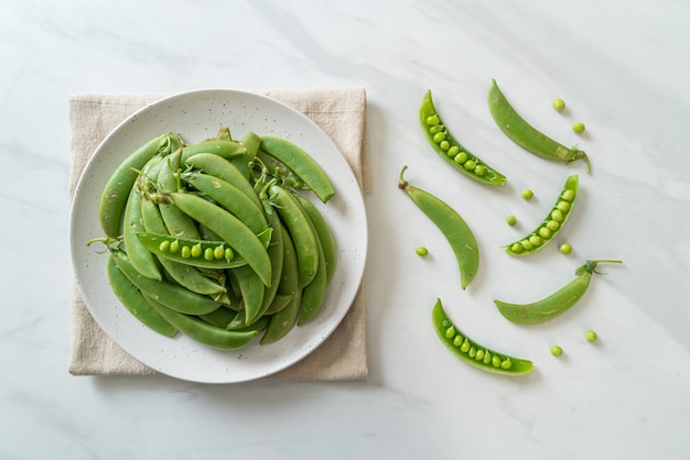 Guisantes verdes dulces frescos en la placa blanca.