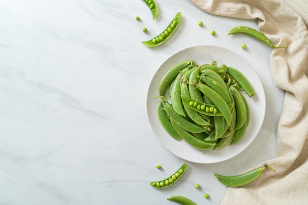 Guisantes verdes dulces frescos en la placa blanca.