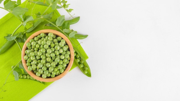 Guisantes verdes frescos en un cuenco de madera con hojas de plantas de guisantes en una servilleta sobre fondo blanco frijol saludable