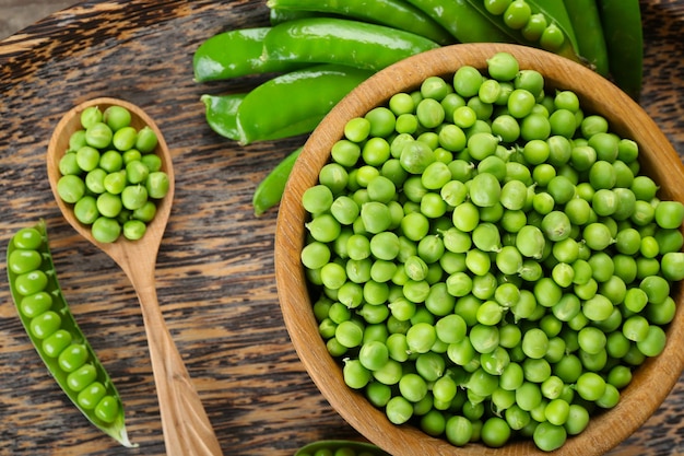 Guisantes verdes frescos en un tazón en la vista superior de la bandeja de madera