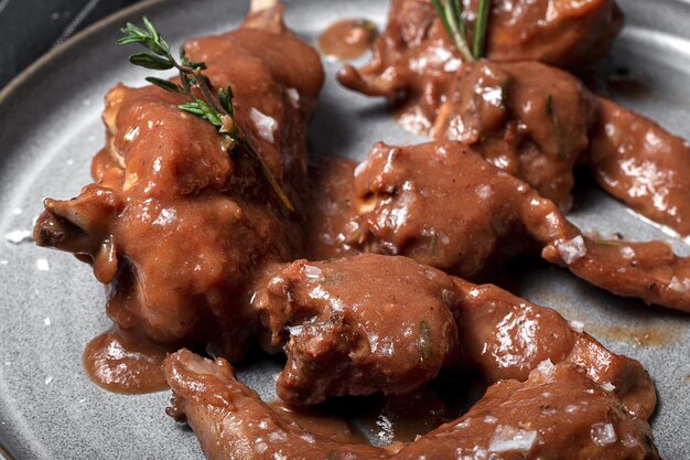 Guiso de carne de conejo casero tradicional con salsa de vino tinto con hierbas aromáticas sobre un fondo negro