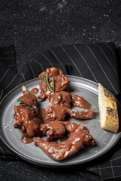 Foto guiso de carne de conejo casero tradicional con salsa de vino tinto con hierbas aromáticas sobre un fondo negro