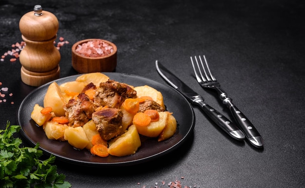 Guiso de carne y verduras de ternera en un plato negro con patatas asadas