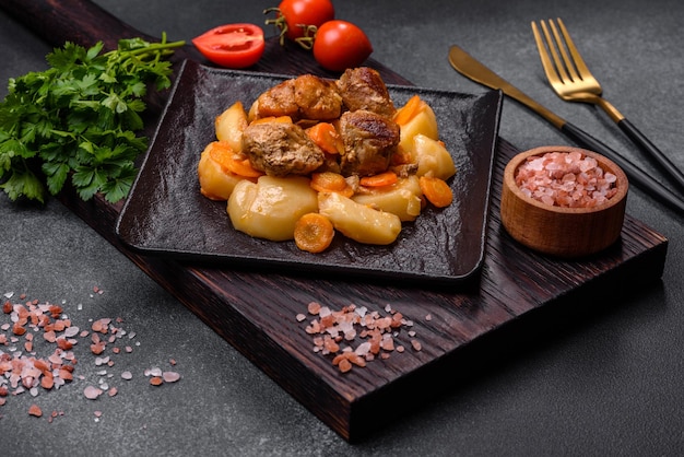 Guiso de carne y verduras de ternera en un plato negro con patatas asadas