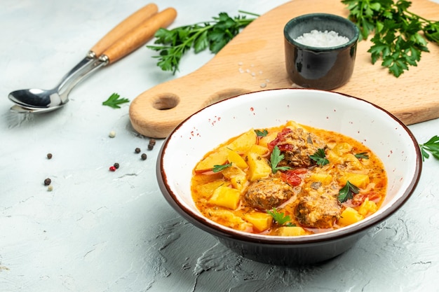 Guiso de verduras con albóndigas, patatas, cebolla, calabacín con salsa de tomate, ajo y hierbas en un recipiente blanco para la vista superior del texto