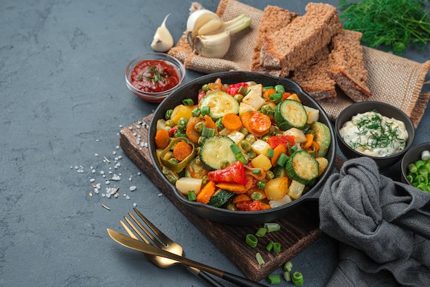 Guiso de verduras saludables, pan de centeno, hierbas y salsas sobre un fondo gris. Vista lateral, espacio para copiar.