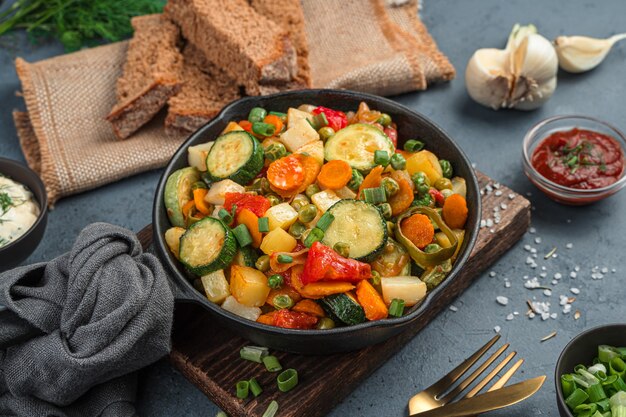 Guiso de verduras en una sartén sobre un fondo gris con pan y ajo. Vista lateral, primer plano.