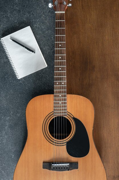 Guitarra acústica y cuaderno de notas sobre un fondo de madera y negro con textura