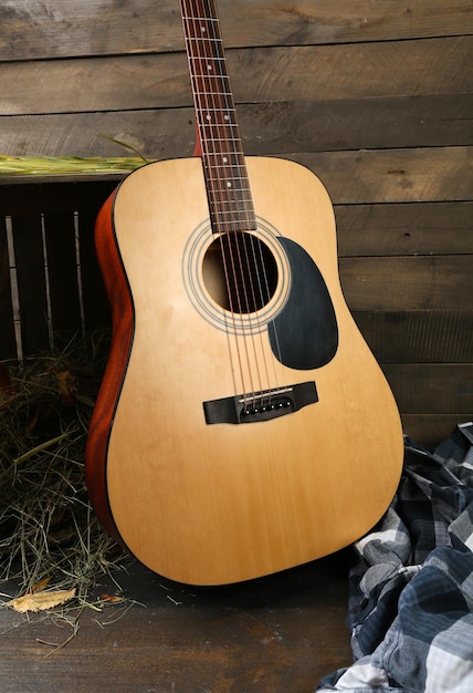 Guitarra acústica e camisa quadriculada azul contra caixa com feno em fundo de madeira