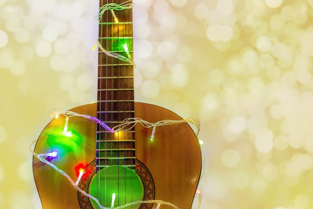 Foto guitarra acústica envuelta por una colorida guirnalda con bokeh. regalo musical de navidad y año nuevo como fondo