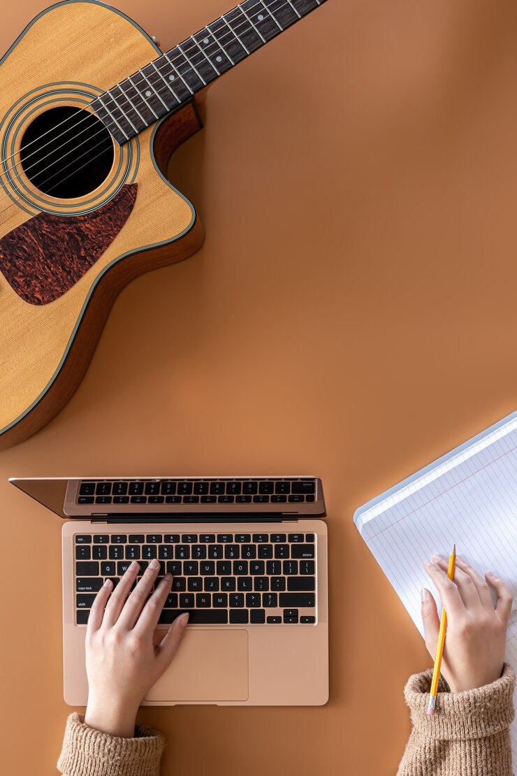 Foto guitarra acústica, manos femeninas trabajan detrás de una computadora portátil, el concepto de crear música.