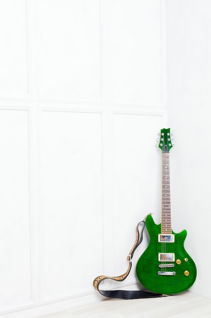 Foto guitarra apoyada frente a una pared blanca.