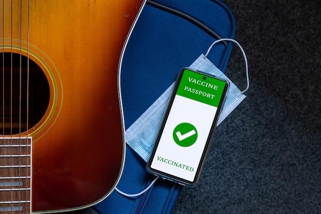 Guitarra, bolso de viaje, mascarilla protectora e identificación de pasaporte de vacuna digital en teléfono móvil. Nuevo concepto de viaje normal
