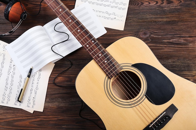 Foto guitarra com fones de ouvido e partituras em fundo de madeira