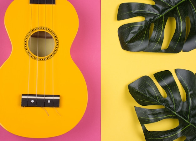 Guitarra de ukulele amarelo brilhante e folhas de monstera