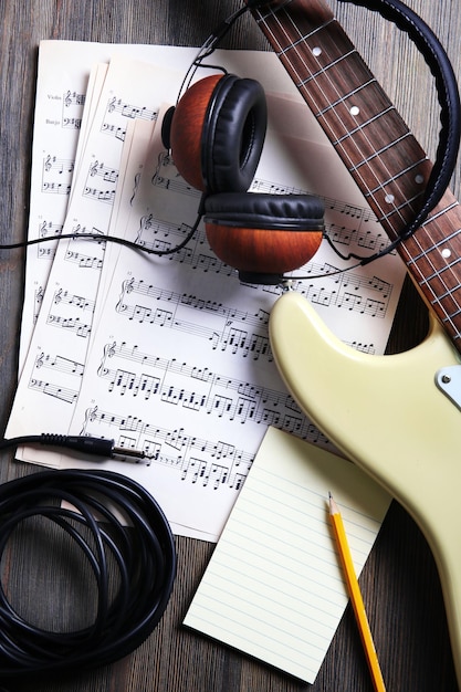 Foto guitarra eléctrica con auriculares y notas musicales sobre fondo de madera