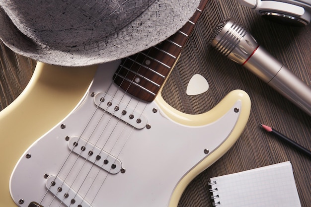 Guitarra eléctrica con auriculares, sombrero y micrófono en un fondo de madera de cerca