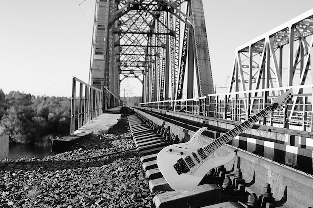 Guitarra eléctrica en blanco y negro en las vías del tren y piedra gris industrial.