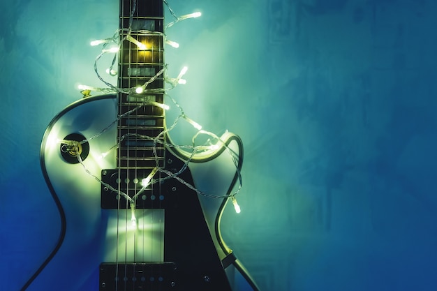 Guitarra eléctrica con guirnalda iluminada sobre fondo azul oscuro. Regala formas clásicas de guitarra para Navidad o año nuevo.