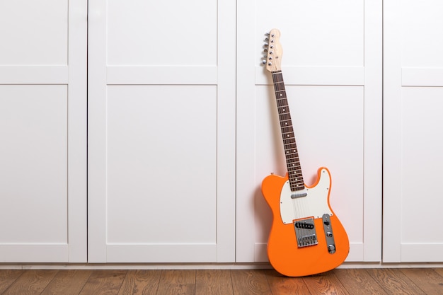 Guitarra eléctrica de pie cerca de la pared blanca en la sala