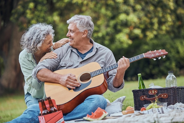 Guitarra musical e um casal sênior em piquenique no parque rindo com comida, bebidas e romance na aposentadoria Amor pela natureza e homem idoso e mulher feliz em encontro romântico na grama no fim de semana de verão