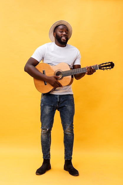 Guitarrista denominado retro afro-americano considerável que joga a guitarra acústica isolada no fundo amarelo.