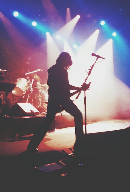 Foto guitarrista em silhueta se apresentando em um palco iluminado durante um concerto de música