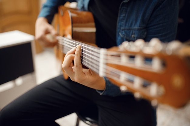 Foto guitarrista masculino tratando de tocar la guitarra acústica en la tienda de música. surtido en la tienda de instrumentos musicales, equipo de compra de músico