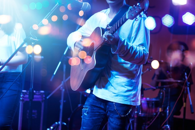 Foto guitarrista no estágio com iluminação para o blackground. guitarrista, macio e conceito do borrão.