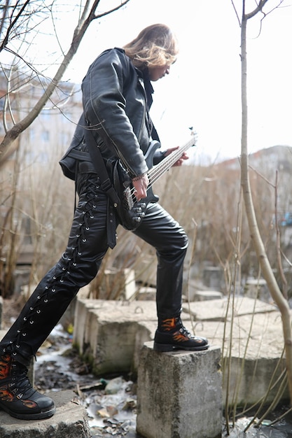 Guitarrista de rock en los escalones. Un músico con un bajo en un traje de cuero. Metalista con una guitarra en el fondo del paso industrial.