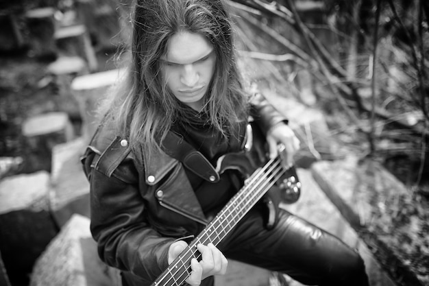 Guitarrista de rock en los escalones. Un músico con un bajo en un traje de cuero. Metalista con una guitarra en el fondo del paso industrial.