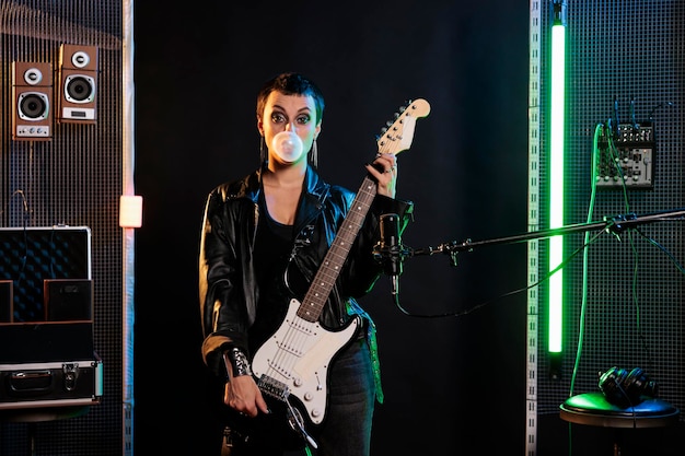 Guitarrista Rockstar segurando guitarra elétrica enquanto toca rock no estúdio de som soprando chiclete. Músico se preparando para realizar um concerto grunge, trabalhando em performance solo