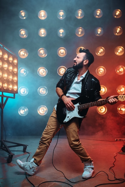 Foto guitarrista solo masculino com guitarra electro no palco com a decoração de luzes.