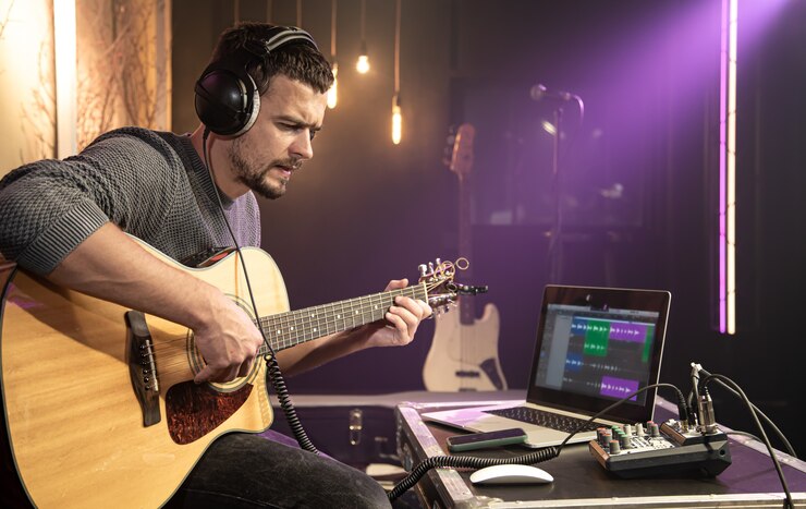 Foto un guitarrista toca la guitarra con auriculares conectados a un mezclador de sonido. forma de onda digital en el monitor de una computadora portátil.